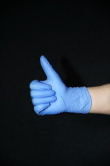  Blue gloved hand, raised thumbs up, closed point, on black background