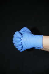  Two blue gloved hands with palms closed against each other, fingers intertwined, on black background