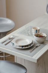 Nicely served dinner plate, knife, spoon and fork, cup and a glass and a bowl of cherries on the dining table.