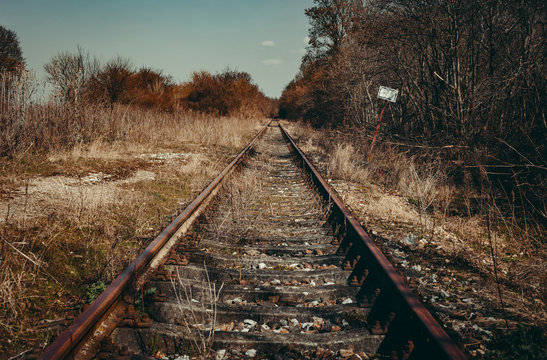 Urbex photo of abandoned, old and damaged train rails in country landscape with blue cloudy sky on background. Train rails crossing dark and old forest in Europe. Vintage photo of rails (wallpaper).