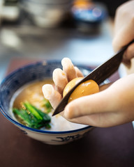 Cook's hand cuts a pickled egg in half, cooking Japanese ramen noodle soup