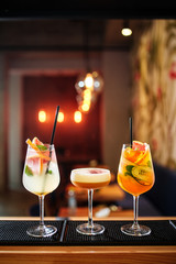 Delicious fruit alcohol cocktails in   glasses with ice, on the bar desk, warm bright lights in the background