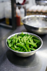 Green edamame soya beans in a metallic bowl on the restaurant kitchen desk, side view, upright, cooking