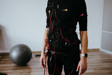 Woman in EMS electro stimulation suit with cables.