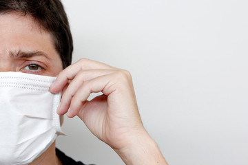 Young man wearing face mask to protect against coronavirus. Indoor photo on white background. Half face close-up.