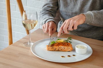 Horizontal close-up of man eating salmon fish steak. Crispy grilled salmon steak with lemon, salad and rosemary, white wine and white sauce.