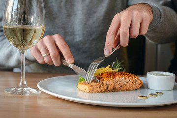 Horizontal close-up of man eating salmon fish steak. Crispy grilled salmon steak with lemon, salad and rosemary, white wine and white sauce.