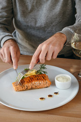 Man eating salmon fish steak with fork an knife. Crispy grilled salmon steak with lemon, salad and rosemary, white sauce. Dinne at the restaurant.