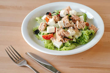 Chicken salad with cherry tomatoes, black olives, cucumber, lettuce. Cesar salad. Concept of a tasty and healthy meal Bright wooden background.