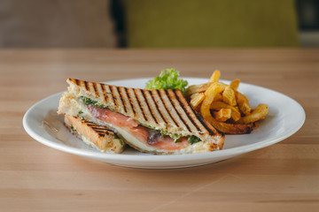 Salmon club sandwiches on white bread, fries and salad on a plate in a restaurant on a wooden table.
