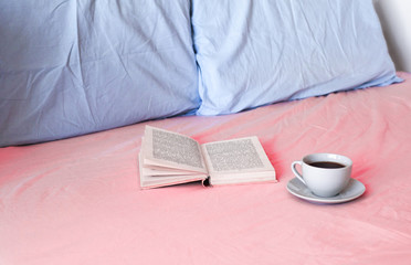 Fototapeta na wymiar book and cup with tea or coffee lie us pink bed with blue pillows 1