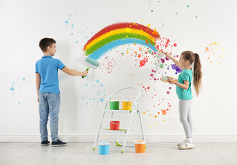 Children drawing rainbow on white wall indoors