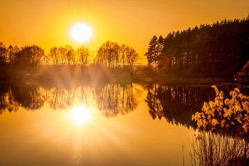 Breathtaking view of the wide angle sunset over the lake with sun reflection and orange sky