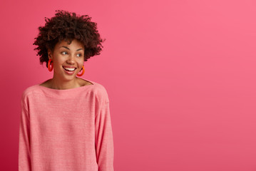 Studio shot of carefree happy Afro American woman looks aside with beaming smile, enjoys nice...