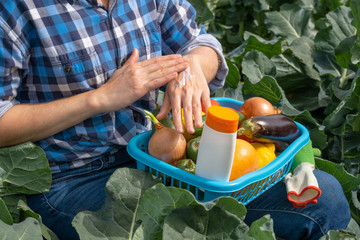 woman works in an agricultural field and smears her hands with sun cream. on a woman lap a basket with vegetables and a white tube with sunscreen