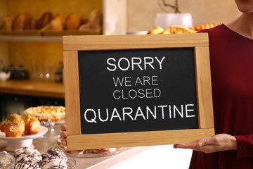 Naklejka na ściany i meble Business owner holding sign with text SORRY WE ARE CLOSED QUARANTINE in bakery, closeup