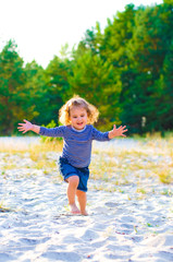 Naklejka premium vertical portrait of a little curly-haired girl running barefoot in the sand