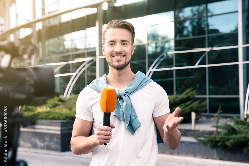 Wall mural Young male journalist with microphone working on city street