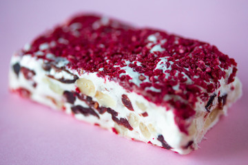 Torrone or nougat bar with nuts and red dried berries. Traditional italian dessert close up on pink background. Sweet tasty and healthy food