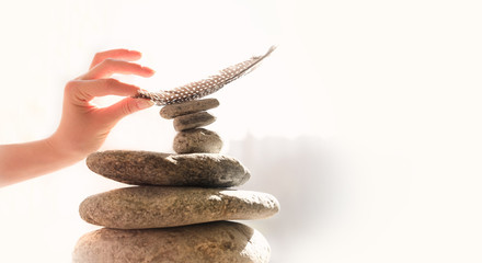 Woman's hand put a feather on a pyramid of stones. Equilibrium, Balance concept. Zen stones on white