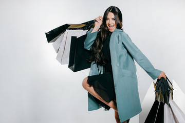 Beautiful young brunette woman holding shopping bags on a grey background. Renewing the wardrobe.