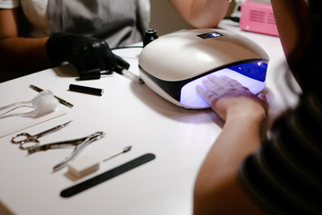 Close-up of the hand of a manicurist who applies gel Polish on the nails of a young girl. Girl dries gel nail Polish in UV lamp.