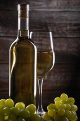 White full wine bottle and wineglass with grapes on a table on a wooden background