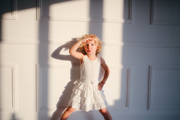 A curly blonde girl in white dress stands like a captain