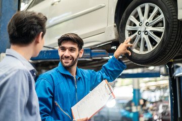 Vehicle maintenance handsome man servicer explain car condition, point at vehicle part to Asian...