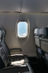 Interior of airplane flying with no passengers. View of an empty row of seats and window. Airplane is banking so you can see the a valley below from the window.