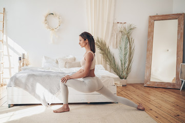 Home fitness. Young sporty fit slim woman doing morning work-out yoga exercises in bedroom at self isolation quarantine. COVID-19 concept to promote stay safe home save lives. Healthy body lifestyle