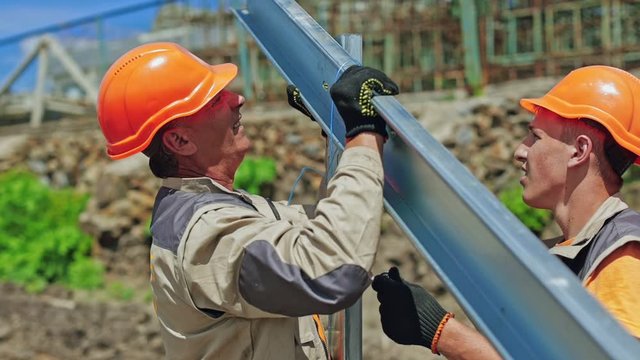 Solar panel technicians install metal frame. Workers in orange helmets making metal basis for solar system on the field. Close-up.