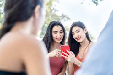 Group of best Asian friends people sitting in outdoor restaurant having meal for lunch together. Young two girls holding and look at mobile phone talking with happiness. Communication & travel concept
