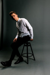 young man sitting on a chair in grey studio in white t-shirt