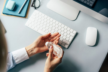 A person treats hands with a disinfector over a working office desk. Self-isolation and hygiene in the epidemic of coronavirus. Stay at home in quarantine and work remotely from home. - Powered by Adobe