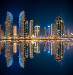Panoramic view with modern skyscrapers and water pier of Dubai Marina at night, United Arab Emirates