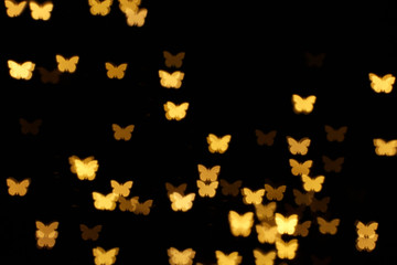Blurred view of butterfly shaped lights on black background. Bokeh effect