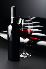 Bottle and glass of red wine on a dark background.