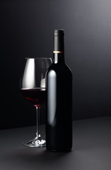 Bottle and glass of red wine on a dark background.