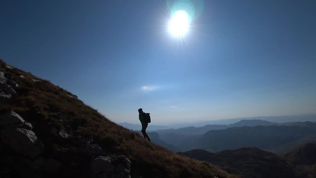 Silhouette of a man with a backpack climbing uphill on the edge of the mountain as a silhouette in a beautiful sunset.