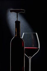 Bottle with corkscrew and glass of red wine.