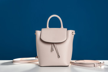 Stylish woman's bag on white table against blue background
