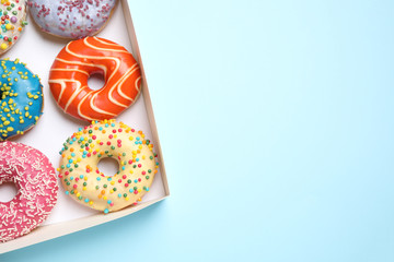 Delicious glazed donuts on light blue background, top view. Space for text
