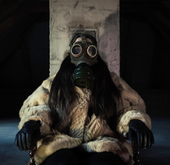 A woman sitting in an attic, wearing a fur coat and gas mask. 