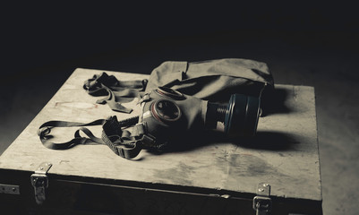 An old military gas mask on a wood box. Side view, flat. Dark background. 