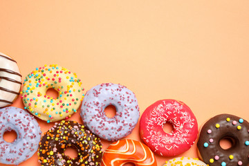 Delicious glazed donuts on orange background, flat lay. Space for text
