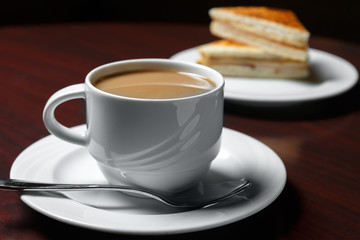 A Cup of coffee on the table against the background of a saucer with cakes