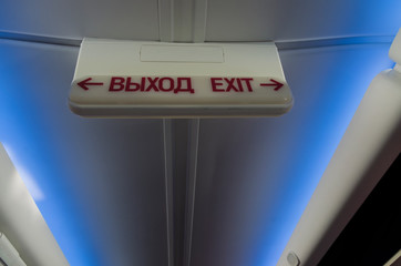 Information luminous sign 'exit' in Russian and English in the plane on the background of the ceiling with a blue light