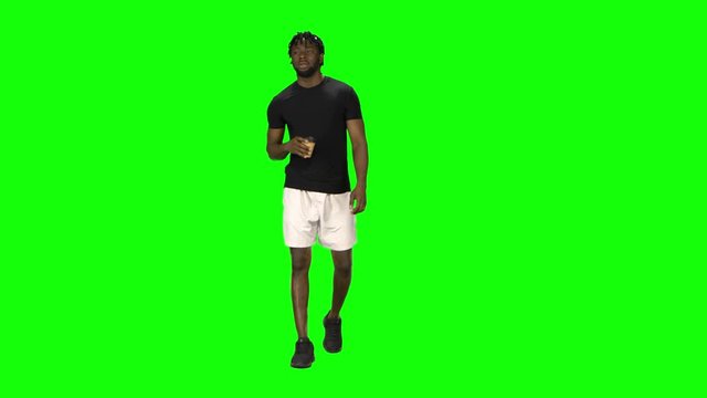 African american man is walking and drinking coffee at Green Screen, Chroma Key. Front view.