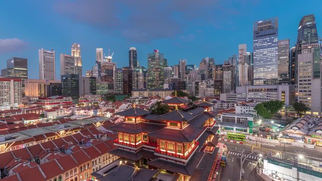 The Buddha Tooth Relic Temple comes alive at night in Singapore Chinatown day to night transition timelapse, with the city skyline in the background. The temple is brightly lit with skyscrapers and